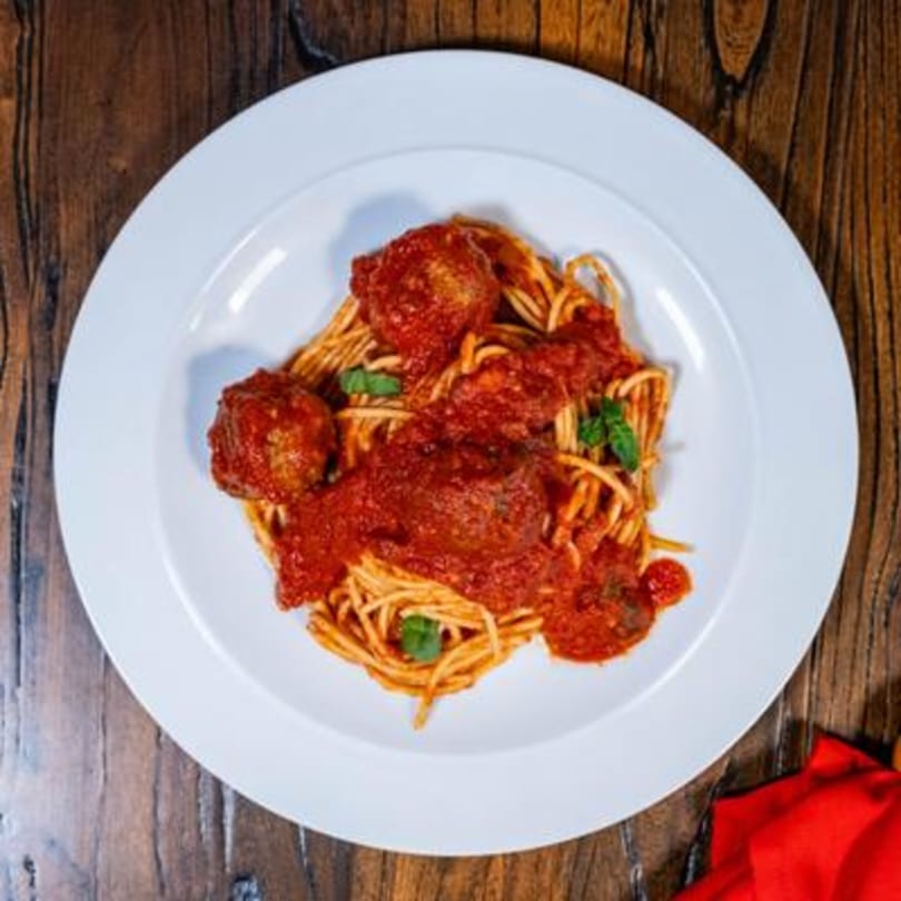 Spaghetti with meatballs and rich red tomato sauce, garnished with fresh basil on a white plate.
