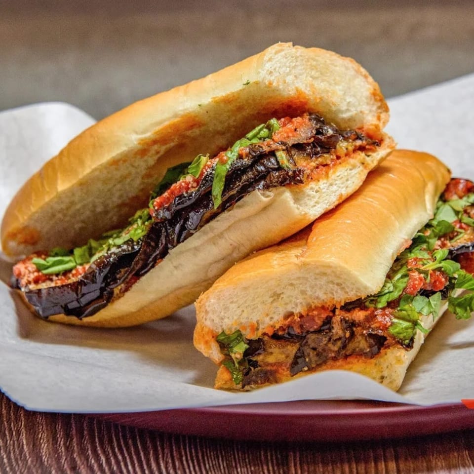 Two eggplant parmesan sandwiches on a white paper-lined red tray, garnished with fresh basil.